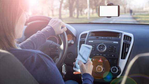 Eine Frau schaut beim Autofahren auf ihr Smartphone.