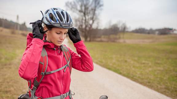 Eine Fahrradfahrerin setzt sich ihren Fahrradhelm auf