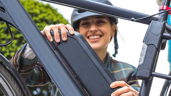 Eine junge Frau hält die Batterie ihres Elektrofahrrades.