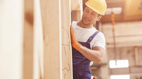 Mann mit Schutzhelm bewegt Holzklotz auf Baustelle