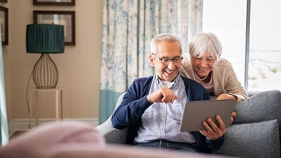 Älteres Paar betrachtet lachend ein Tablet