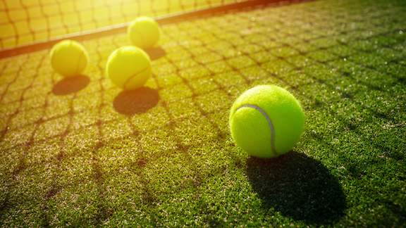 Tennisbälle liegen im Sonnenschein vor einem Tennisnetz
