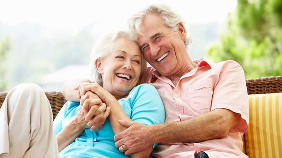 Ein älteres Ehepaar sitzt lachend auf einer Bank