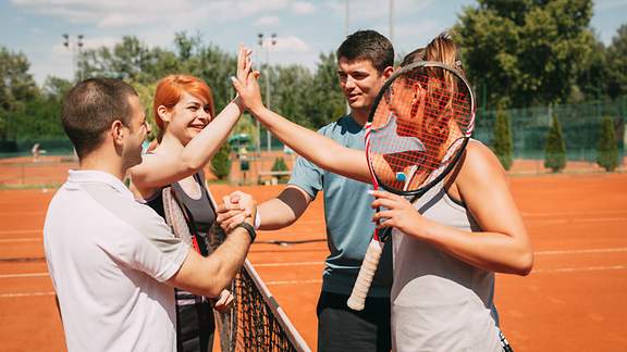 Zwei gemischte Tennis-Doppel klatschen am Netz ab