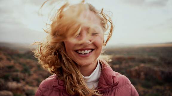 Junge Frau mit vom Winde verwehten Haaren lacht mit geschlossenen Augen