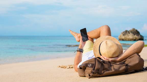 Mann mit Smartphone liegt am Strand