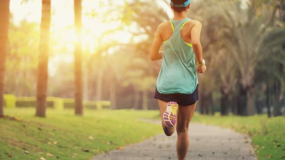 Eine junge Frau joggt durch den Park (Rückenansicht)