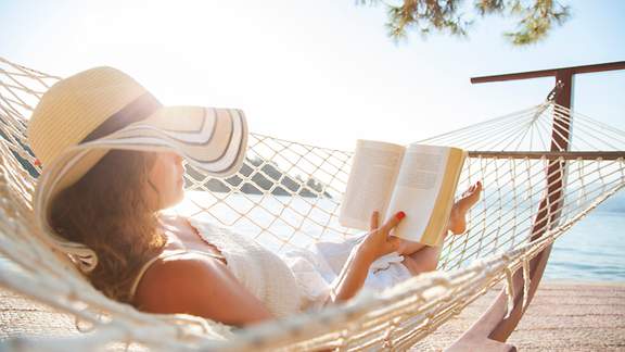 Frau in einer Hängematte mit Buch im Urlaub