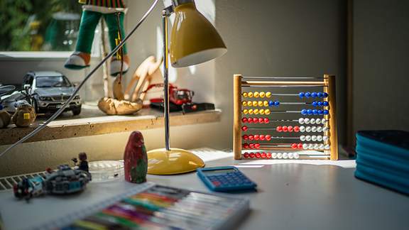 Der Schreibtisch in einem Kinderzimmer mit einer Lampe, Malstiften und enem Rechenschieber