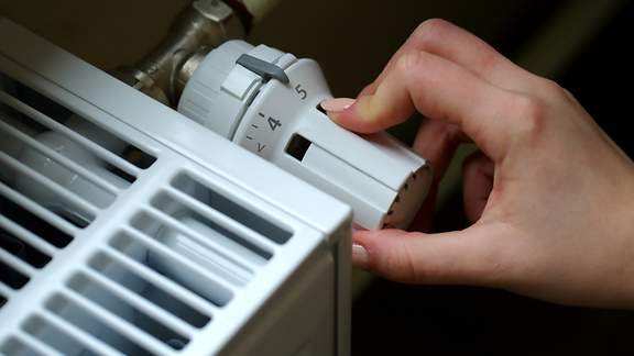 Eine Hand dreht am Thermostat einer Heizung
