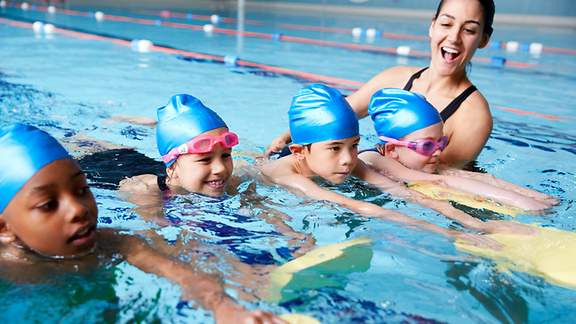 Schwimmtrainerin mit vier jungen Schwimmanfängern im Becken