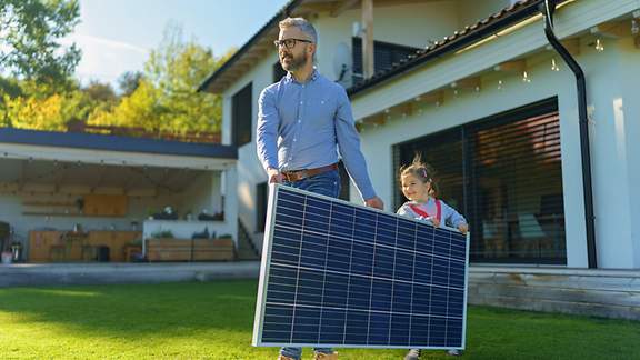 Vater und Tochter tragen ein Solarmodul durch den Garten