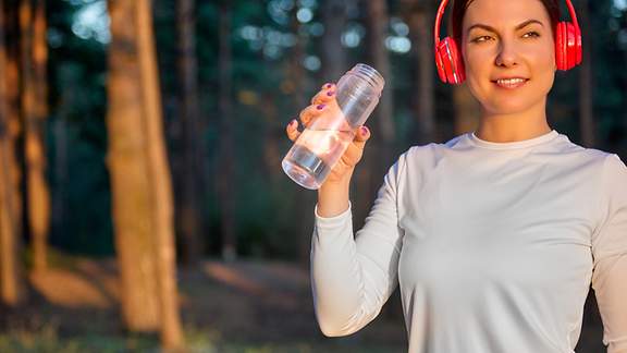 Nahaufnahme einer Sportlerin nach dem Training mit Kopfhörern, die eine Flasche Wasser in den Händen hält