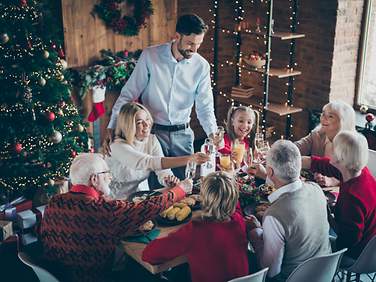 Familienmitglieder aus drei Generationen sitzen gemeinsam vor einem geschmückten Weihnachtsbaum