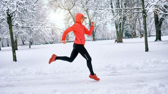 Läuferin mit rotem Oberteil auf Schnee im Park an einem sonnigen Wintertag