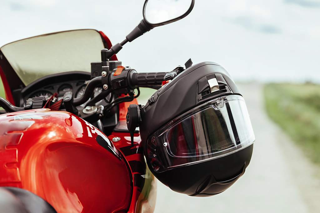 Ein rotes Motorrad steht auf einer ländlichen Straße, während der schwarze Helm an einem Griff baumelt 