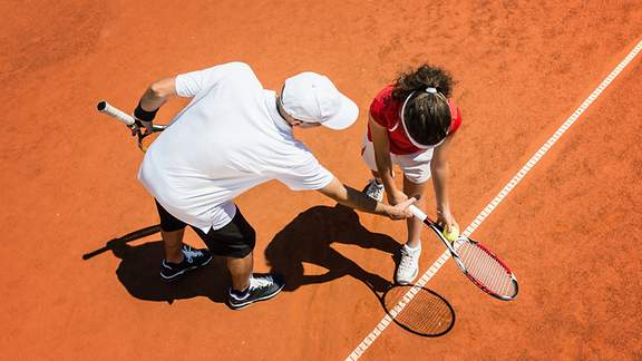 Tennislehrer korrigiert die Schlägerhaltung seiner Schülerin